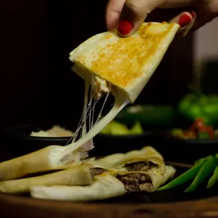a person holding a piece of cheese over a tortilla