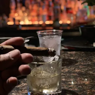 a person holding a cigar and a glass of alcohol