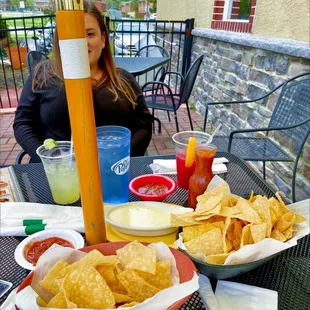 a woman sitting at a table with chips and drinks
