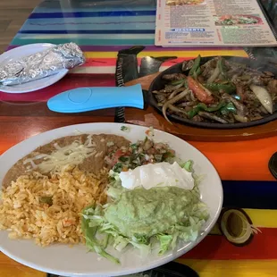 Sizzling fajitas with rice, beans, lettuce, pico de gallo, sour cream, guacamole, tortillas