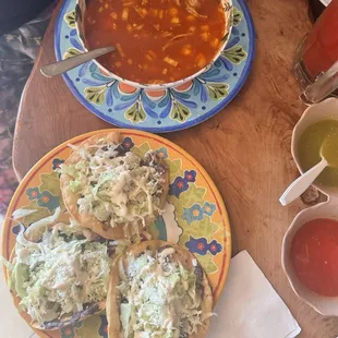 A bowl of Posole and 3 tostadas with beans, lettuce, cheese and crema.