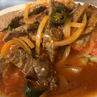 Bistec Ranchero Steak chunks, cooked in ranchero sauce served with rice, beans and salad.