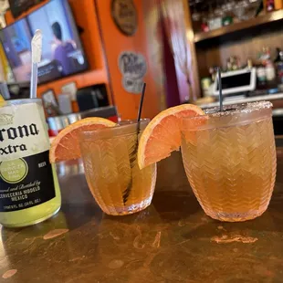 two glasses of orange juice and a bottle of corona extra
