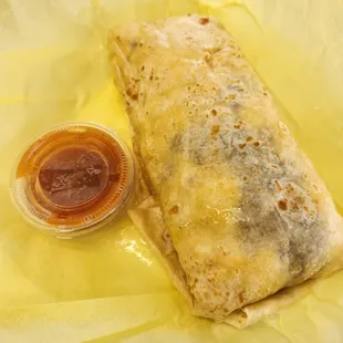 Machaca and egg burrito compared to the salsa container. Note the oil or grease on the wrapper and tortilla.
