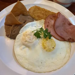 Eggs, hash browns "look store bought " and a thin slice of ham and what looks like a deli cut slice from a package .