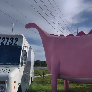 a pink dinosaur next to a food truck