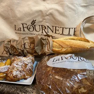 Mini lemon madeleines, almond croissants, Miche Sourdough Bread, a Baguette, and an extra tall canvas tote.