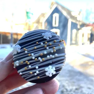 a hand holding a chocolate donut with white and gold sprinkles
