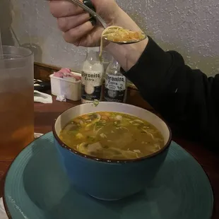 a person holding a spoon over a bowl of soup