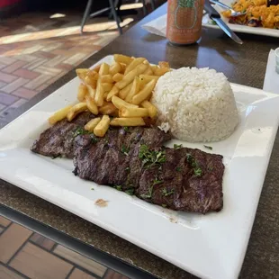 a plate of steak, rice, and french fries