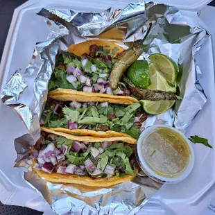 three tacos in foil with a side of salsa