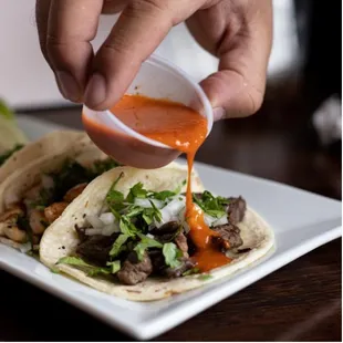 a hand drizzing sauce onto a taco