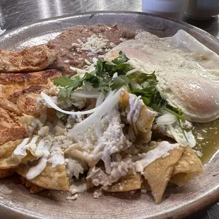 Chilaquiles verdes con huevos estrellados, pollo y frijoles.