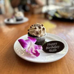 a chocolate cupcake on a plate with a flower