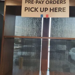 Sign on shelf stating to pick up orders &quot;here.&quot;