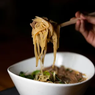 a person holding chopsticks over a bowl of noodles