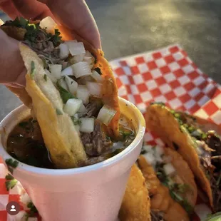 a person dipping a piece of meat into a bowl of soup