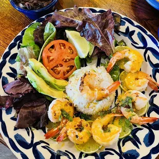 a plate of food with shrimp, rice, lettuce, tomato, and avocado