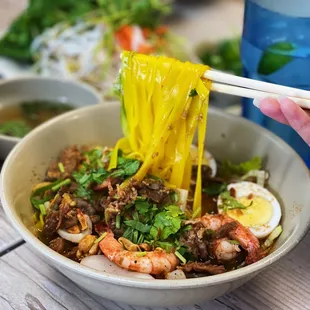 a person holding chopsticks over a bowl of noodles