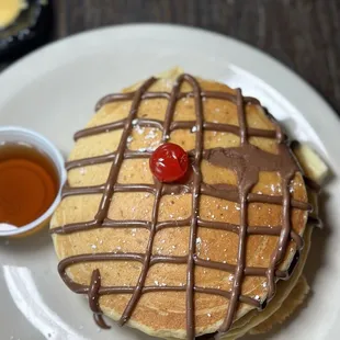 a stack of pancakes with chocolate drizzle and a cherry on top