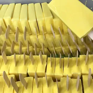 a person holding a spatula over a tray of yellow popsicles
