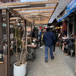 people walking down a sidewalk with tables and chairs