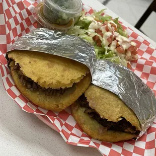 a sandwich wrapped in aluminum foil with a side salad