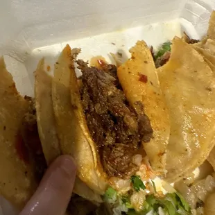 a hand grabbing a piece of food from a styrofoam container