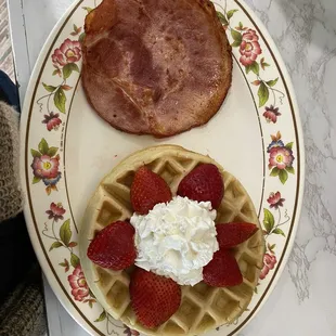 a plate of waffles with strawberries and bacon