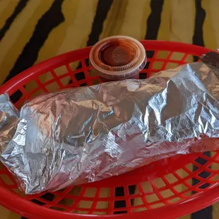 a burrito wrapped in aluminum foil with a side of ketchup