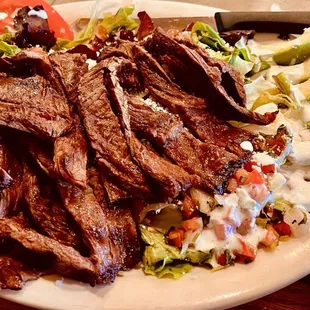 Carne Asada Salad with slices tomatoes and avocados on a bed of lettuce with ranch dressing.