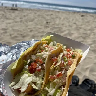 a hand holding a taco on the beach