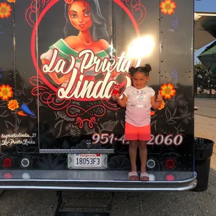 a little girl standing in front of a food truck