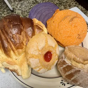 Clockwise from top: Purple concha, orange concha w/sugar crystals, corn bread w/sugar, cookie, giant not-a-croissant but delicious.