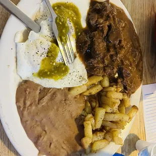 Carne Guisada, two eggs over easy, potatoes, refried beans and flour tortillas. Salsa Verde.