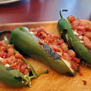 three stuffed jalapenos on a cutting board