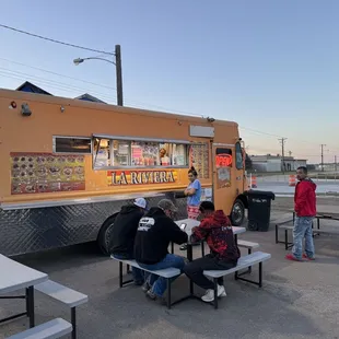 a group of people sitting at picnic tables in front of a food truck