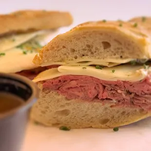 The &quot;French Dip&quot; served on a house-baked baguette, featuring sliced roasted beef, smoked mozzarella, charred onion aioli au jus for dipping.