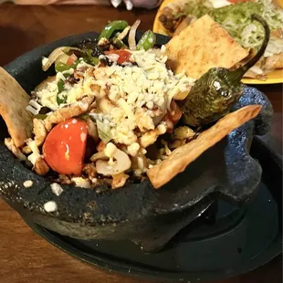 Molcajete filled with chicken steak, shrimp, grilled onions, tomatoes, and pepper in a red sauce