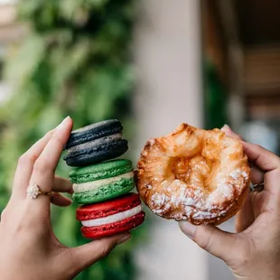 a hand holding a donut and a stack of macarons