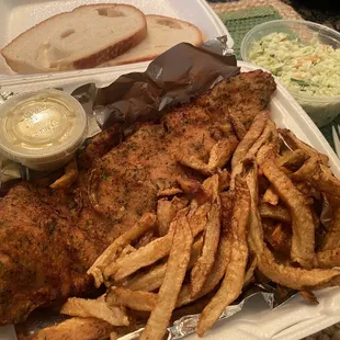 Fried haddock dinner with French fries, cole slaw and two slices of italian bread.