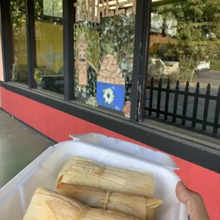 a person holding a container of tamales
