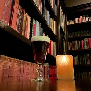 a glass of beer and a candle in front of a bookshelf