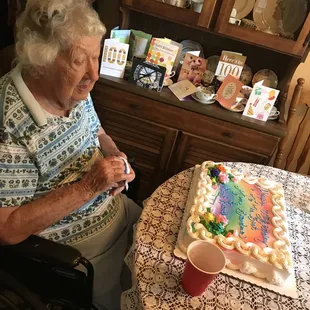 an elderly woman sitting at a table with a birthday cake