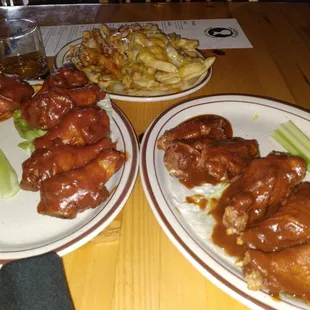 two plates of chicken wings, celery, and fries