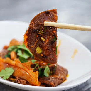 a piece of meat being lifted by chopsticks