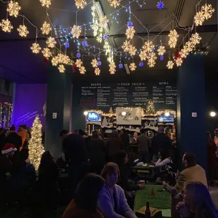a crowd of people sitting in a room with snowflakes hanging from the ceiling