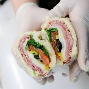 a gloved hand holding a cut in half sandwich