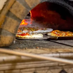 two pizzas cooking in a brick oven