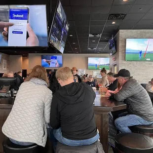 people sitting at a bar watching tvs